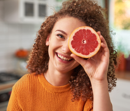 Healthy young woman holding a cut grapefruit covering her eye